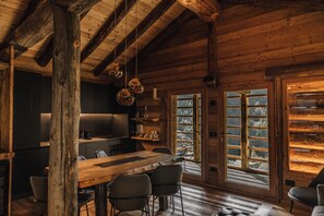 A rustic wooden interior with a dining area, kitchen, and large windows offering a view of a snowy landscape. - ad maiora baita walser chalet with spa (alagna valsesia)