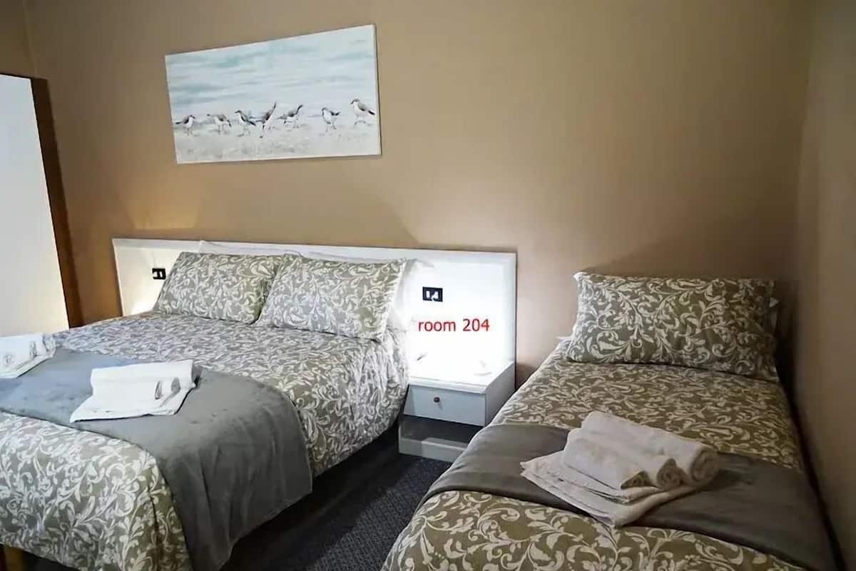 A hotel room with two beds, each with a pillow and a blanket. There is a painting on the wall above the beds, and a sign indicating the room number 204.