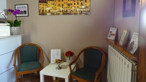 A room with two wooden chairs, a small table, a vase with flowers, and a framed cityscape painting on the wall. - affittacamere arancio (Lucca)