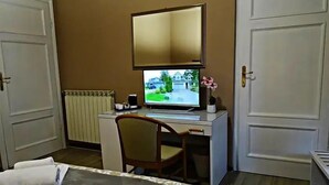 A hotel room with a bed, a desk with a computer, a chair, a radiator, and a door. - affittacamere arancio (Lucca)