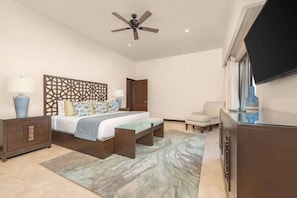 A bedroom with a bed, bedside tables, a ceiling fan, a TV, and a view of a building outside.