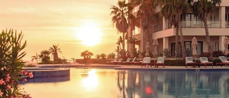 A pool area with lounge chairs and palm trees, reflecting the sunset.