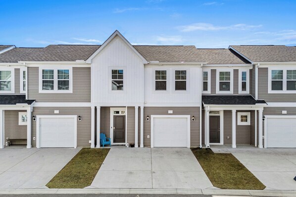 A row of townhouses with attached garages, a central entrance, and a small front yard. - 3BR, Outdoor Movie Theatre, Indoor Fireplace, Arcades, 5 Minutes from Beach! (Little River)