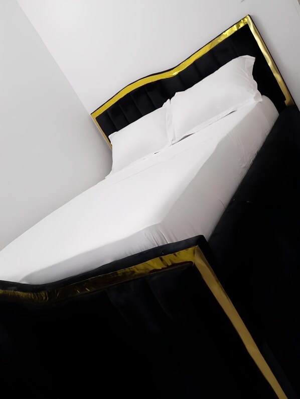 Una cama con estructura negra y dorada, ropa de cama blanca y cabecera negra.