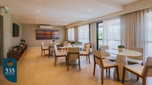 Un comedor amplio con mesas y sillas redondas, un sofá y un televisor montado en la pared.