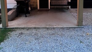 A covered outdoor area with a concrete floor, a wooden bench, and a string of lights. - Relax & unwind in this country cottage near the Muskingum River & State Parks.  (Mcconnelsville)