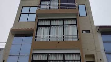 A multi-story building with large windows, a balcony, and solar panels on the roof.
