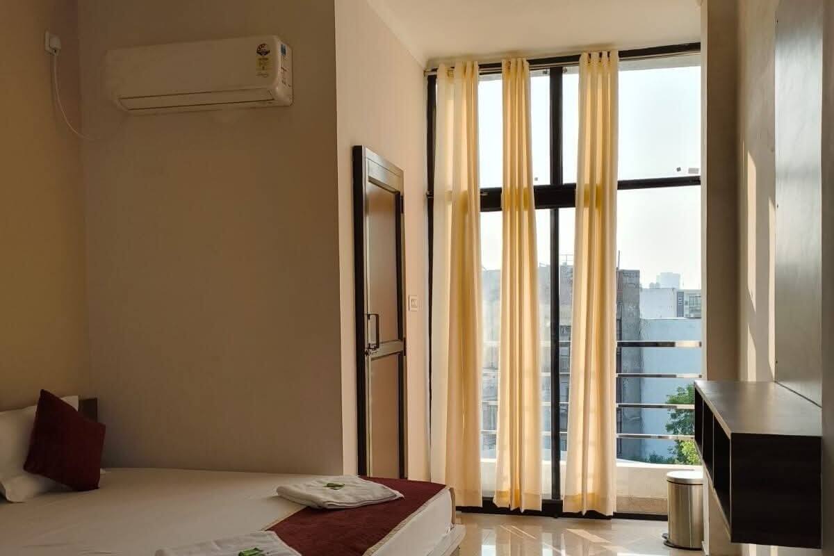 Une chambre d’hôtel avec un lit, un bureau, une chaise, une télévision et une fenêtre avec des rideaux.