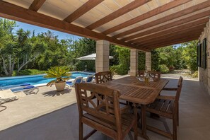 Relax and dine under the shade of a pergola, surrounded by lush greenery and a serene pool.