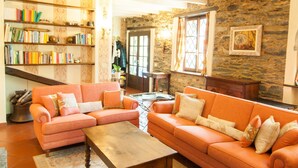 Ein gemütliches Wohnzimmer mit Holzbalkendecke, orangefarbenen Sofas, einem Couchtisch und einem Bücherregal voller Bücher.