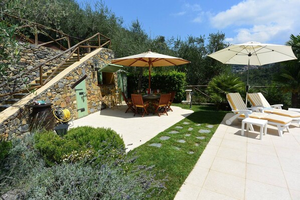 A stone staircase leading to a patio with a table and chairs, surrounded by lush greenery and a pool area with lounge chairs. - The Grapefruit House - Villa con Piscina (Garlenda)