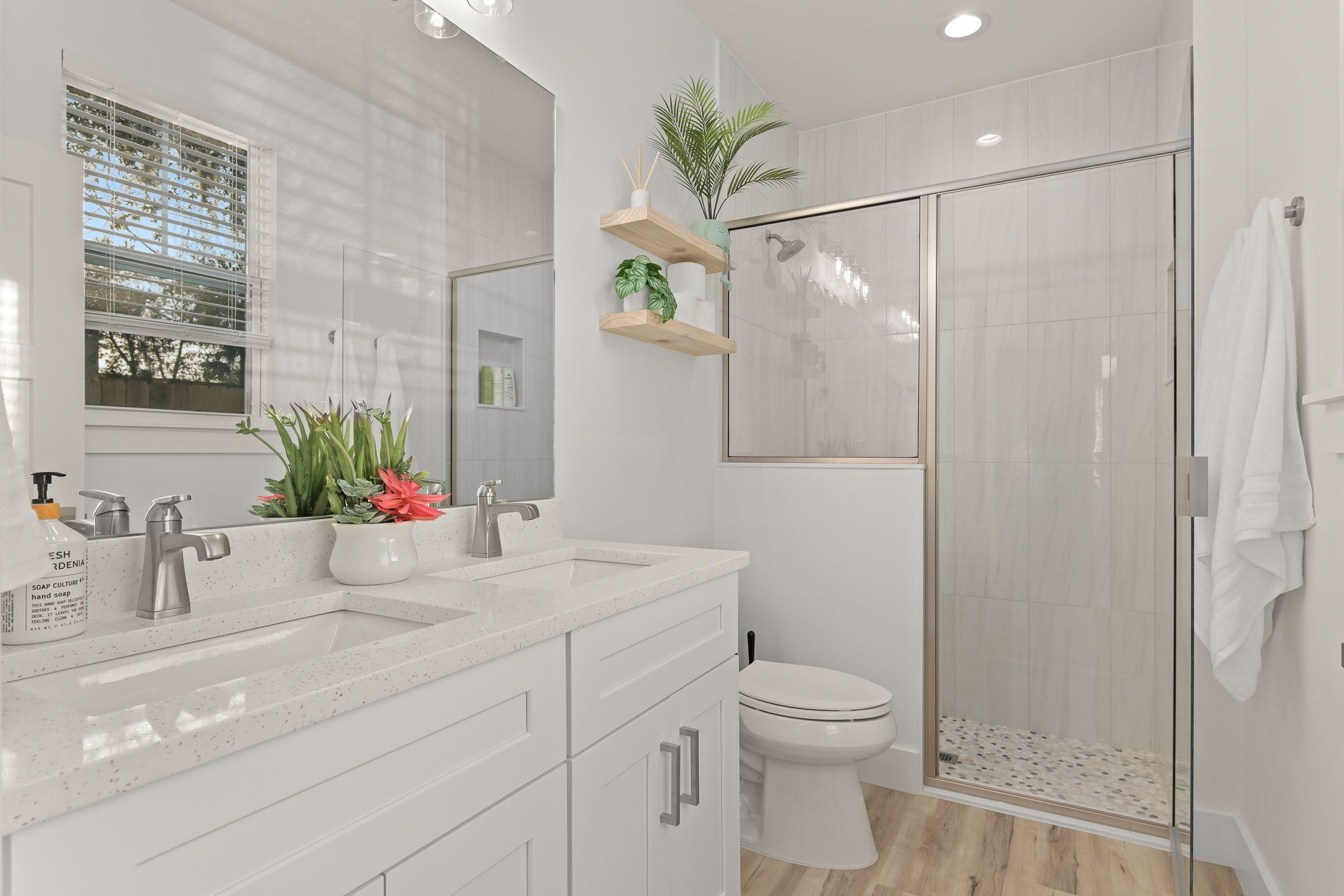 A modern bathroom with a glass-enclosed shower, white cabinetry, and a potted plant on a shelf.