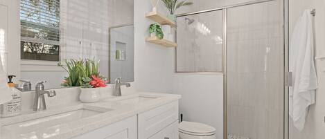 A modern bathroom with a glass-enclosed shower, white cabinetry, and a potted plant on a shelf.