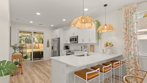 A modern kitchen with white cabinets, a central island with stools, and pendant lighting. - Sunshine Duo: Two Coastal Homes Blocks Apart, Sleeps 13, 1mi to Downtown (St. Augustine)