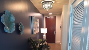 A hallway with a chandelier, a potted plant, a lamp, and a door with louvered glass. - Gorgeous Lush 2 Bedroom Condo with Amazing Views and Endless Amenities (Orange Beach)