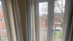 Una sala de estar con un sofá a cuadros, una silla de madera y un amplio ventanal corredera con vistas a una zona residencial.