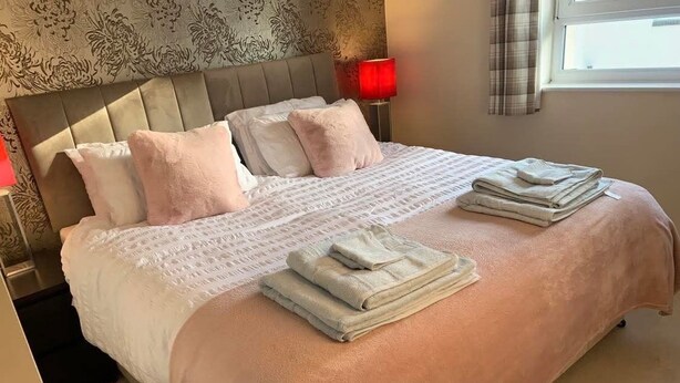 Una cama bien hecha con una manta rosa, almohadas y toallas dobladas.