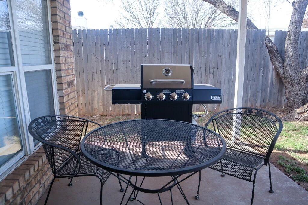 Een achtertuin met een barbecue, twee metalen stoelen en een houten omheining.