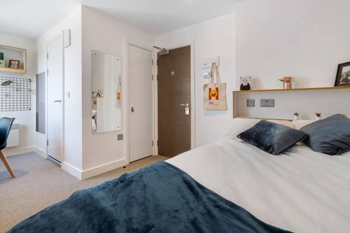 A hotel room with a bed, a desk, a chair, a wardrobe, and a door.