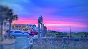 A sunset view with a boardwalk, cars, and buildings in the background. - Gorgeous 4 BR with Ocean Views & Pool (Kure Beach)