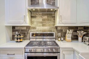 A kitchen with a stainless steel stove, a digital control panel, a backsplash with tiles, and a set of knives on the counter. - Stylish Home with Pool Table & 2 Outdoor Spaces - Walkable (Houston)