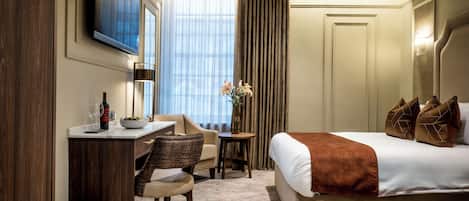 Ein Hotelzimmer mit einem Bett, einem Schreibtisch mit Stuhl, einem an der Wand montierten Fernseher und einem Fenster mit Vorhängen.