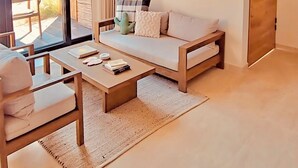 A modern living room with a sofa, coffee table, and chairs. There is a large window with a view of a garden. A macrame wall hanging is visible. - Sunny Bungalow with a Pool and Near the Beach (El Pescadero)