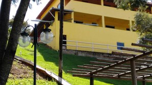 A yellow building with a metal railing and a grassy area in front. - Sítio Sonho Real (Taquaraçu de Minas)