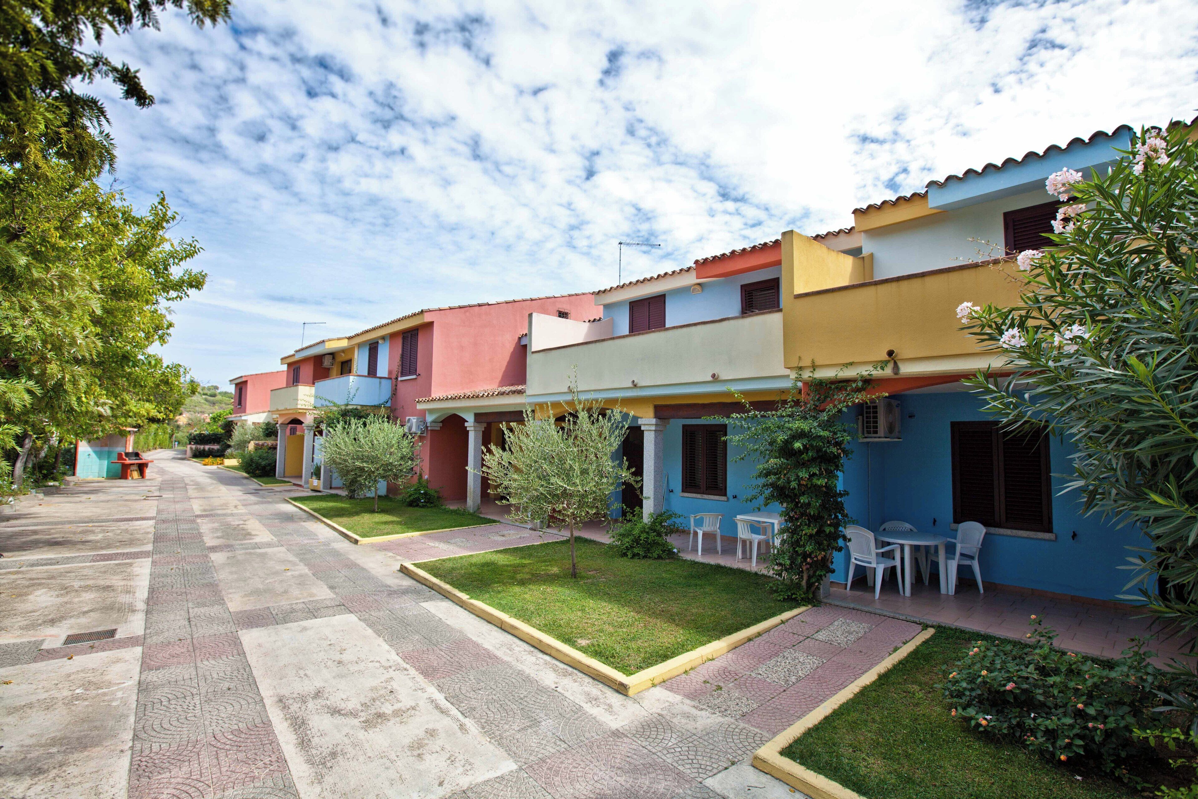 A row of colorful buildings with a paved walkway and small trees.