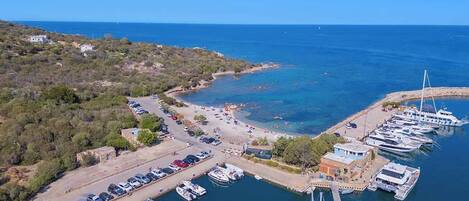 An aerial view of a marina with boats docked, a parking area, and a small building.