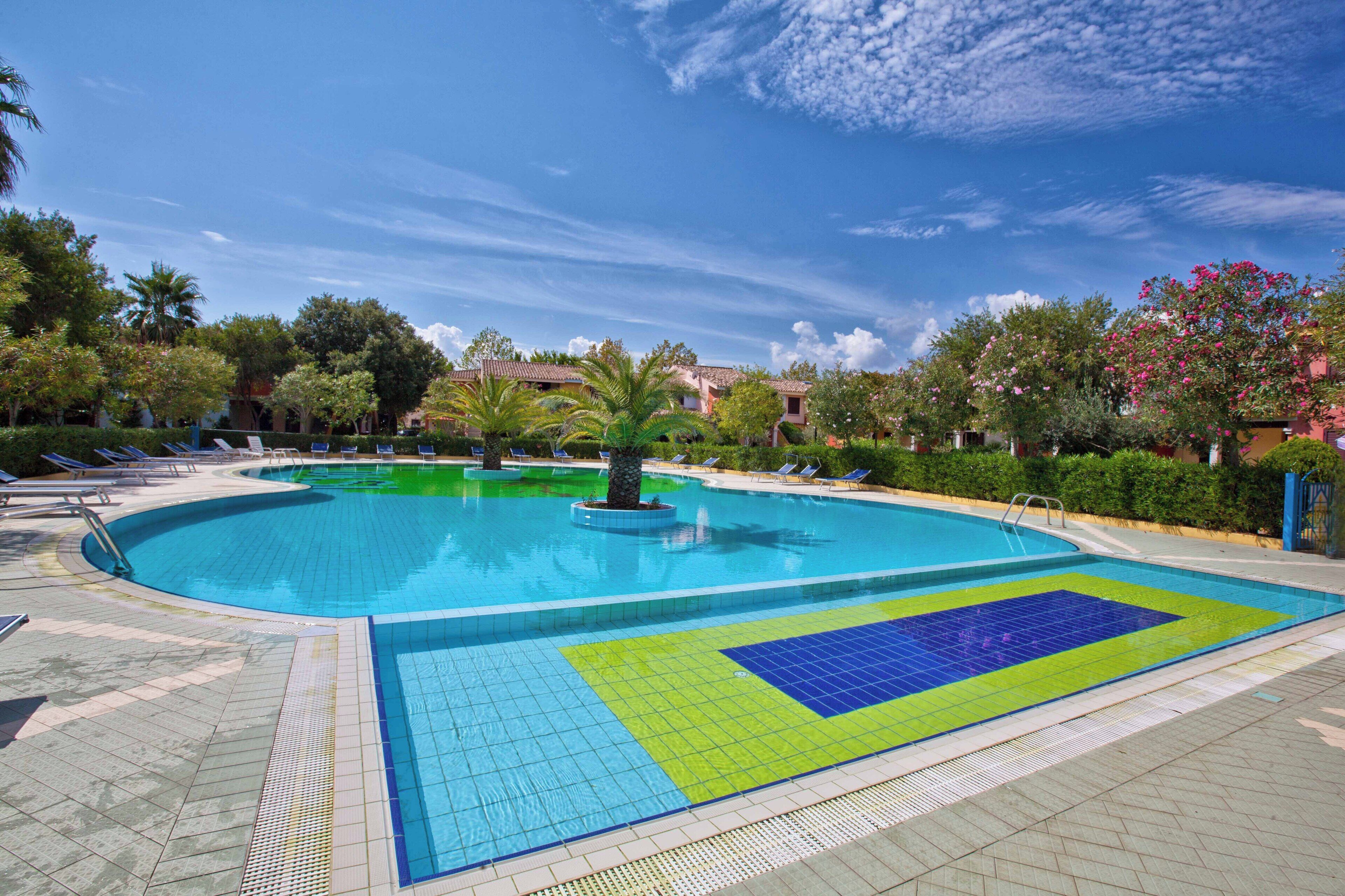 Ein Swimmingpool mit gefliestem Sonnendeck, umgeben von Liegestühlen und Palmen.