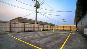 An outdoor tennis court with yellow boundary lines, surrounded by a wooden fence and utility poles. - 5 min. to Lincoln's top attractions. 2 Queens, WiFi, pickleball, & outdoor space (Lincoln)