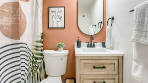 A bathroom with a toilet, sink, mirror, and a framed picture on the wall.