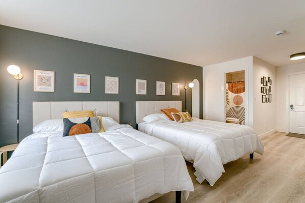 Ett hotellrum med två sängar, en grå vägg och inramade konstverk.