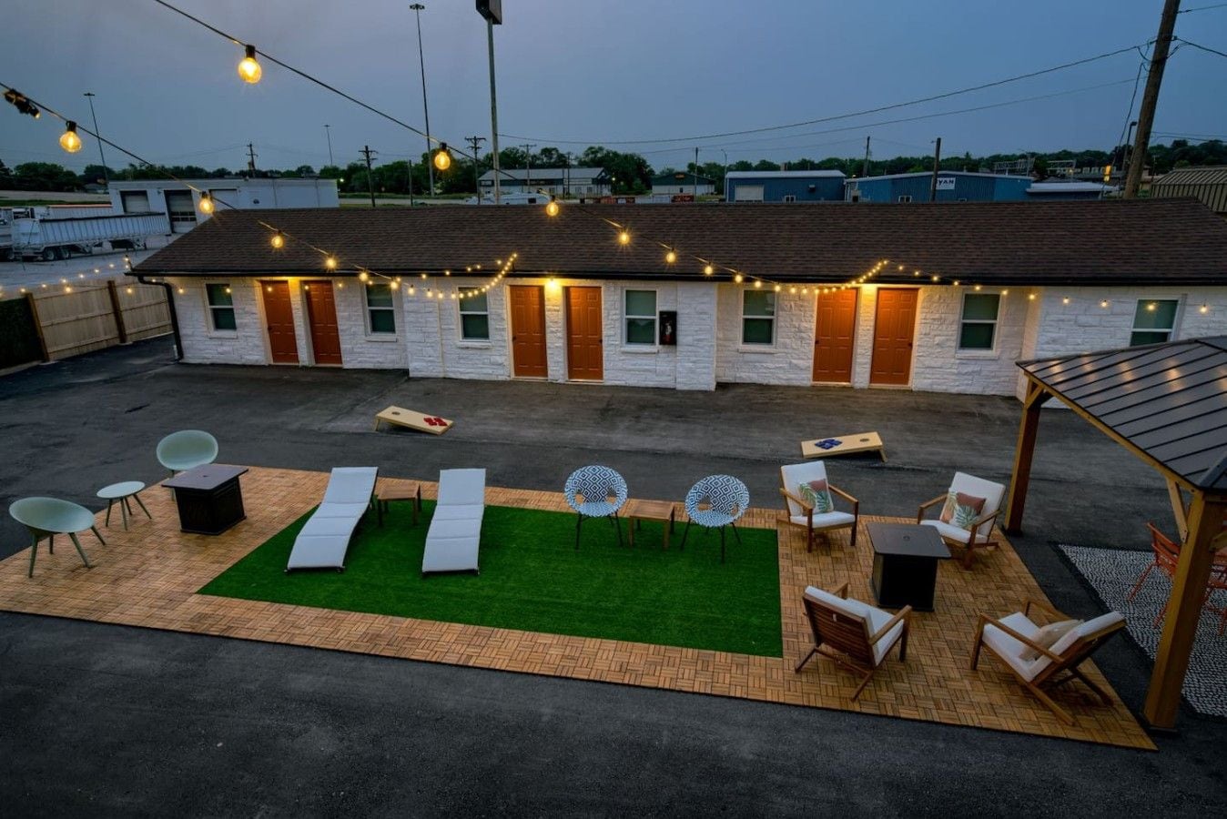 Un patio en la azotea con mobiliario exterior, un pequeño jardín y luces colgantes.