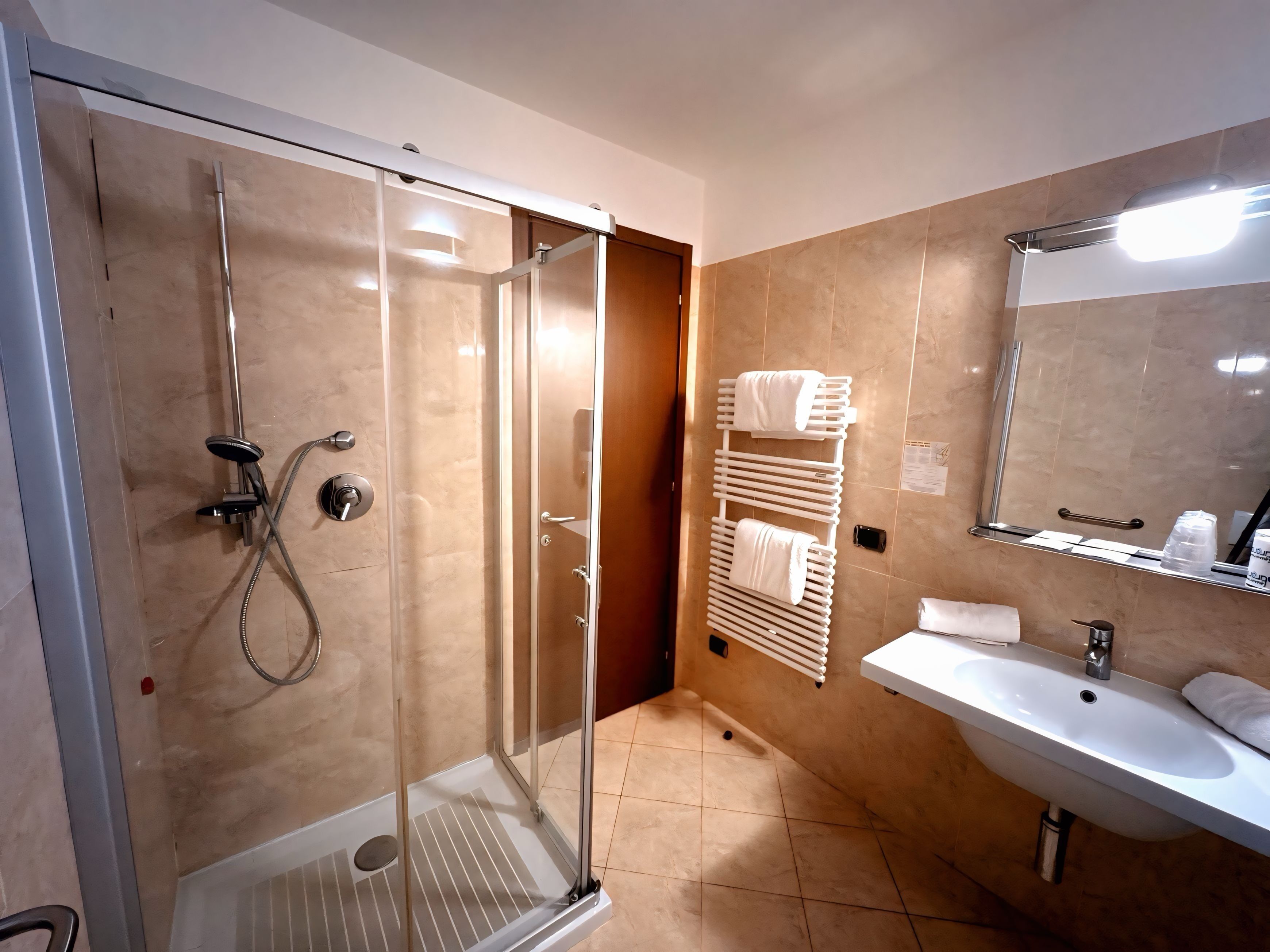 Un baño moderno con ducha de vidrio, un lavamanos blanco y un perchero para toallas.