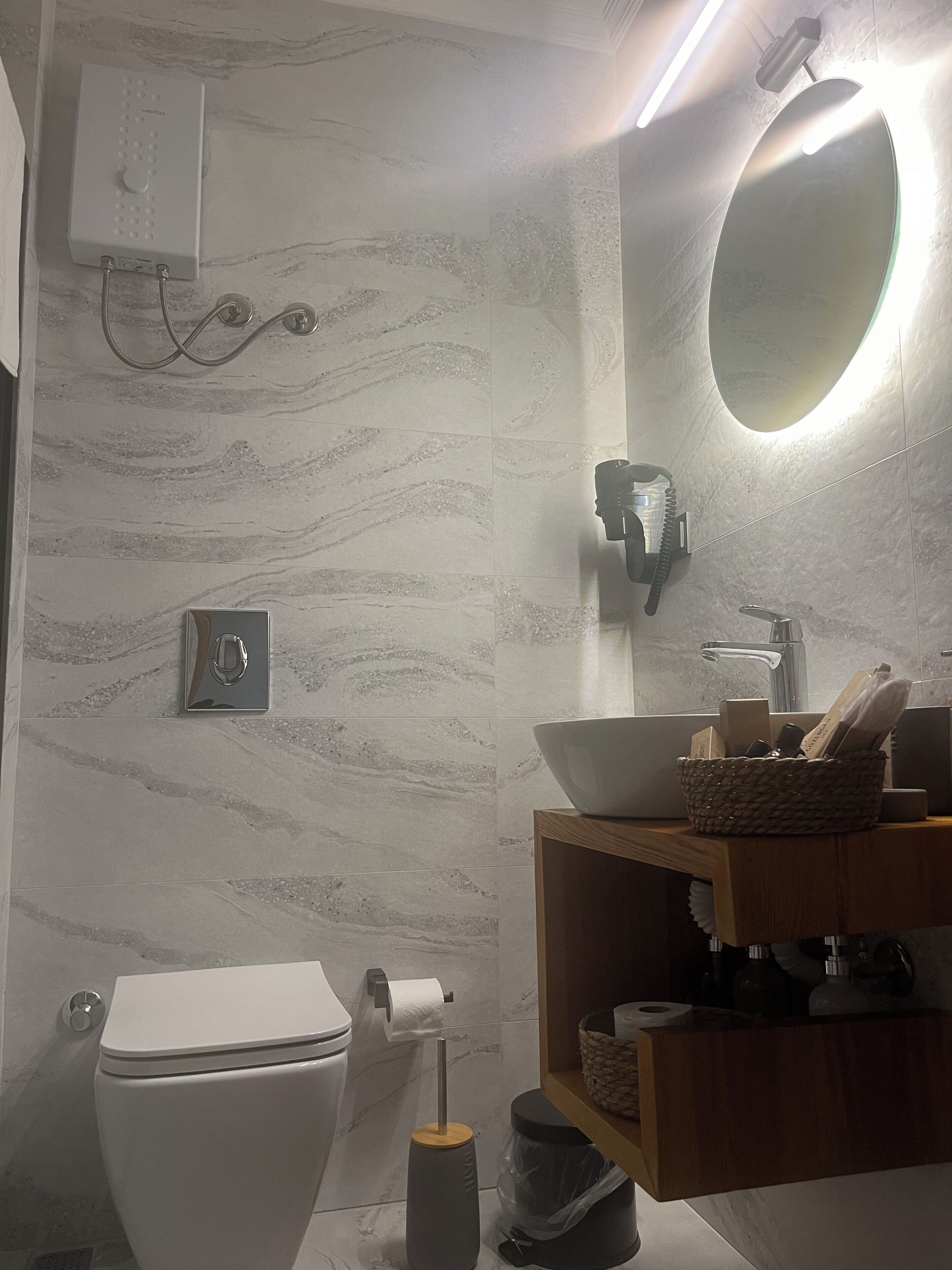 A modern bathroom with a toilet, bidet, vanity with a mirror, and a wall-mounted light fixture.