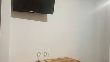 Uma sala de estar com televisão de tela plana fixada na parede, um rack de madeira com copos e um aparelho de ar condicionado.