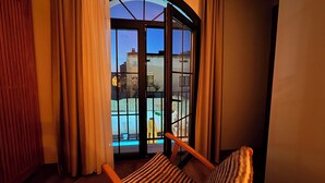 A room with a sliding glass door leading to a pool area, a wooden chair, and a view of buildings outside. - Güzergah Urla (Urla)