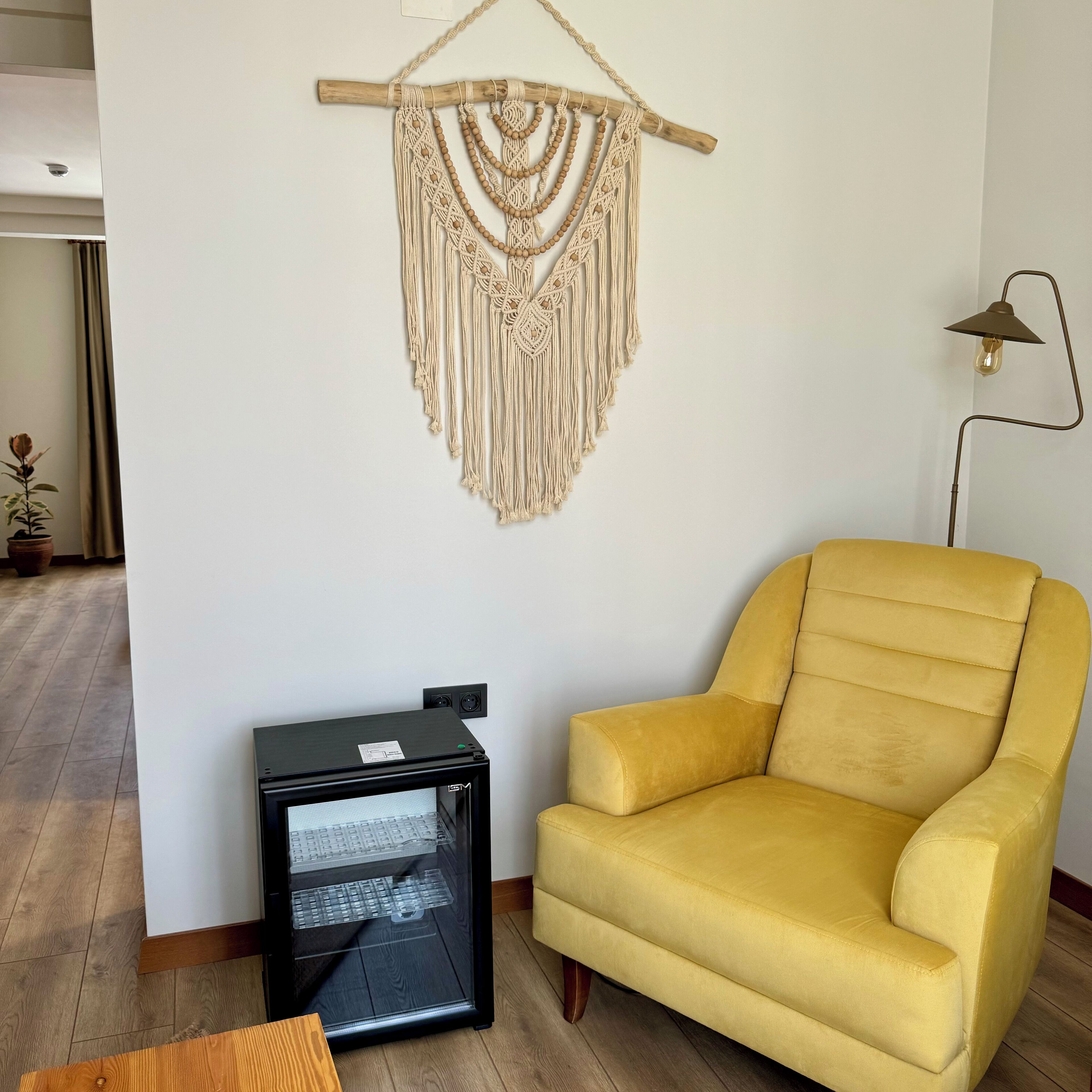 A yellow armchair, a macrame wall hanging, a black cabinet, and a floor lamp.