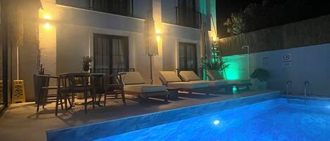 A modern building with a swimming pool, outdoor seating, and ambient lighting.