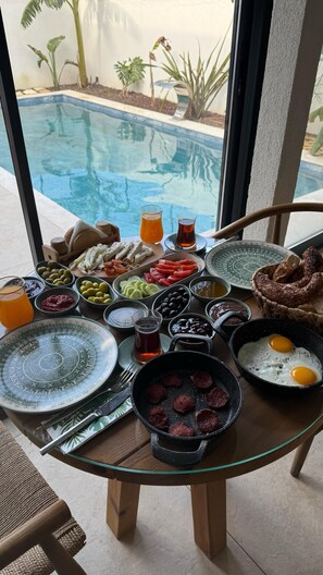 A breakfast table with various dishes, a pool view, and a glass table. - Güzergah Urla (Urla)