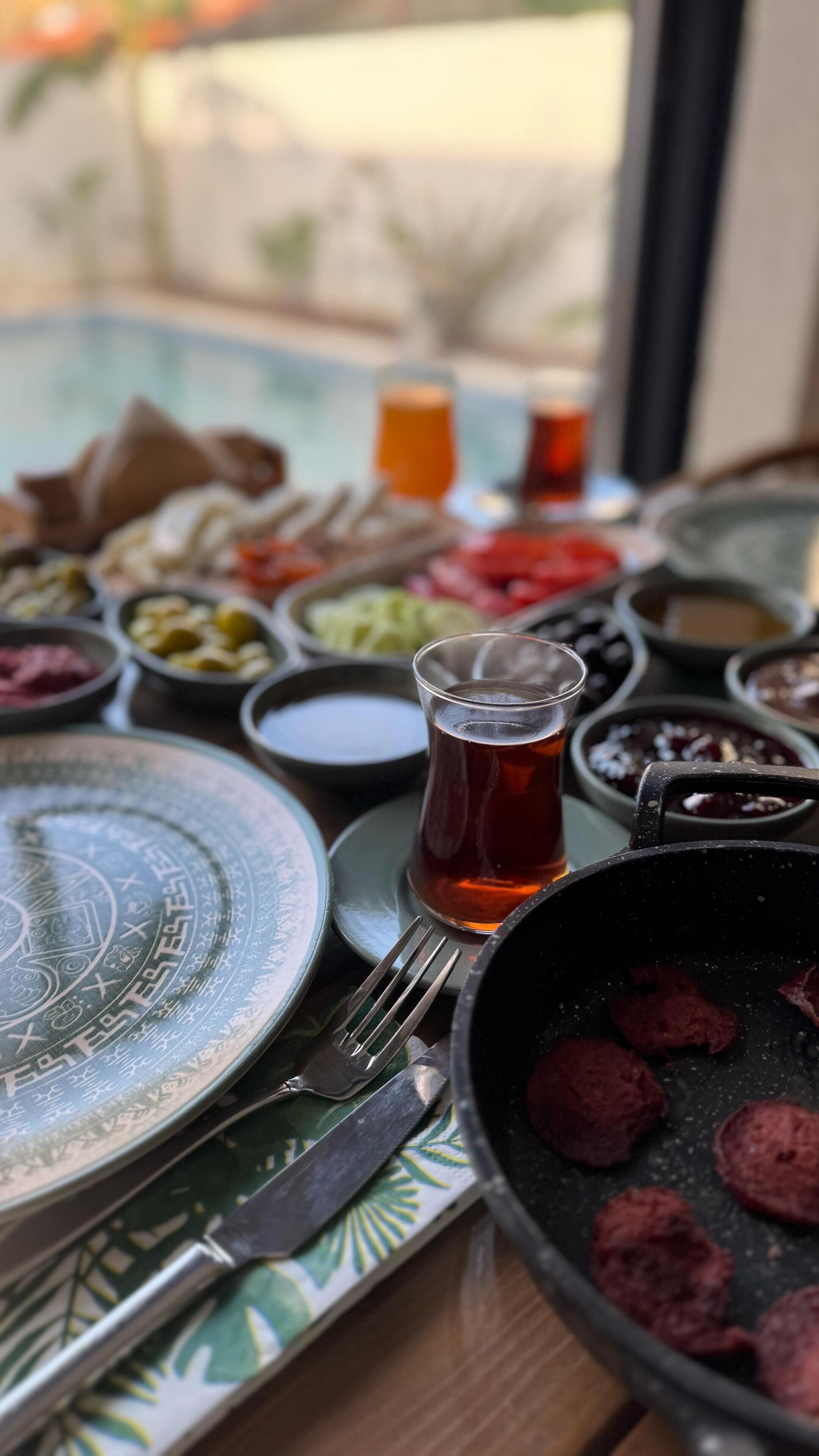A table set with various dishes, a glass of tea, and a view of the outdoors.