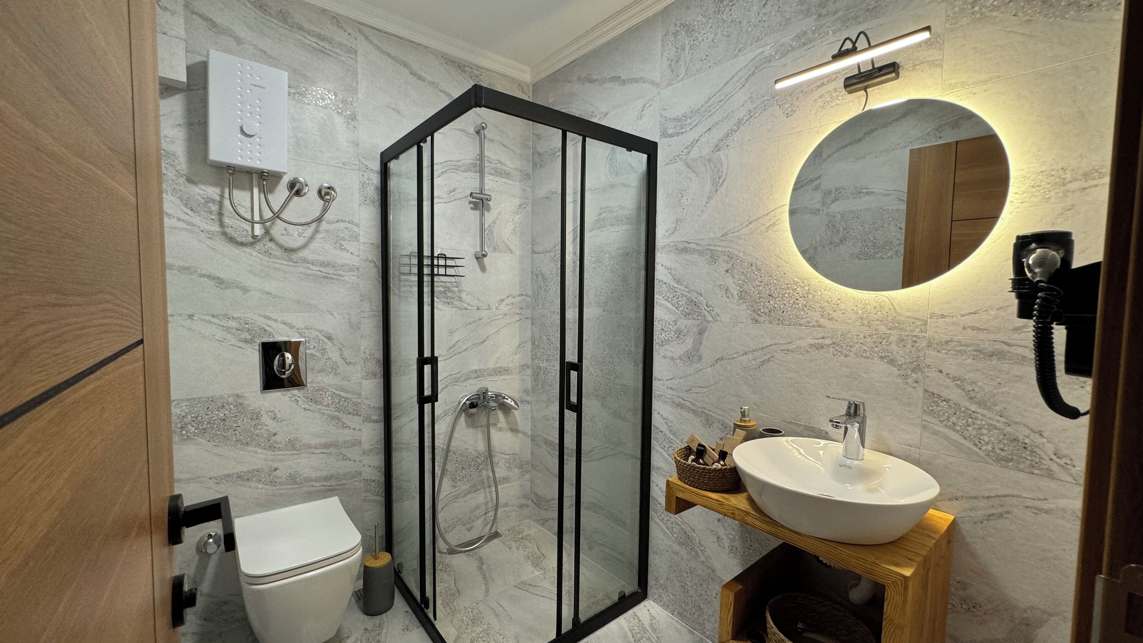 Un baño moderno con ducha de vidrio, un lavabo blanco y un inodoro.