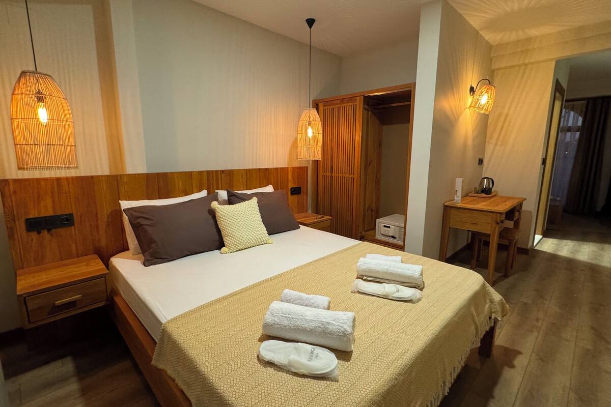 A hotel room with a wooden headboard, a bed with white linens, two bedside tables, a wooden nightstand, a bedside lamp, a wooden desk with a chair, and a mirror.