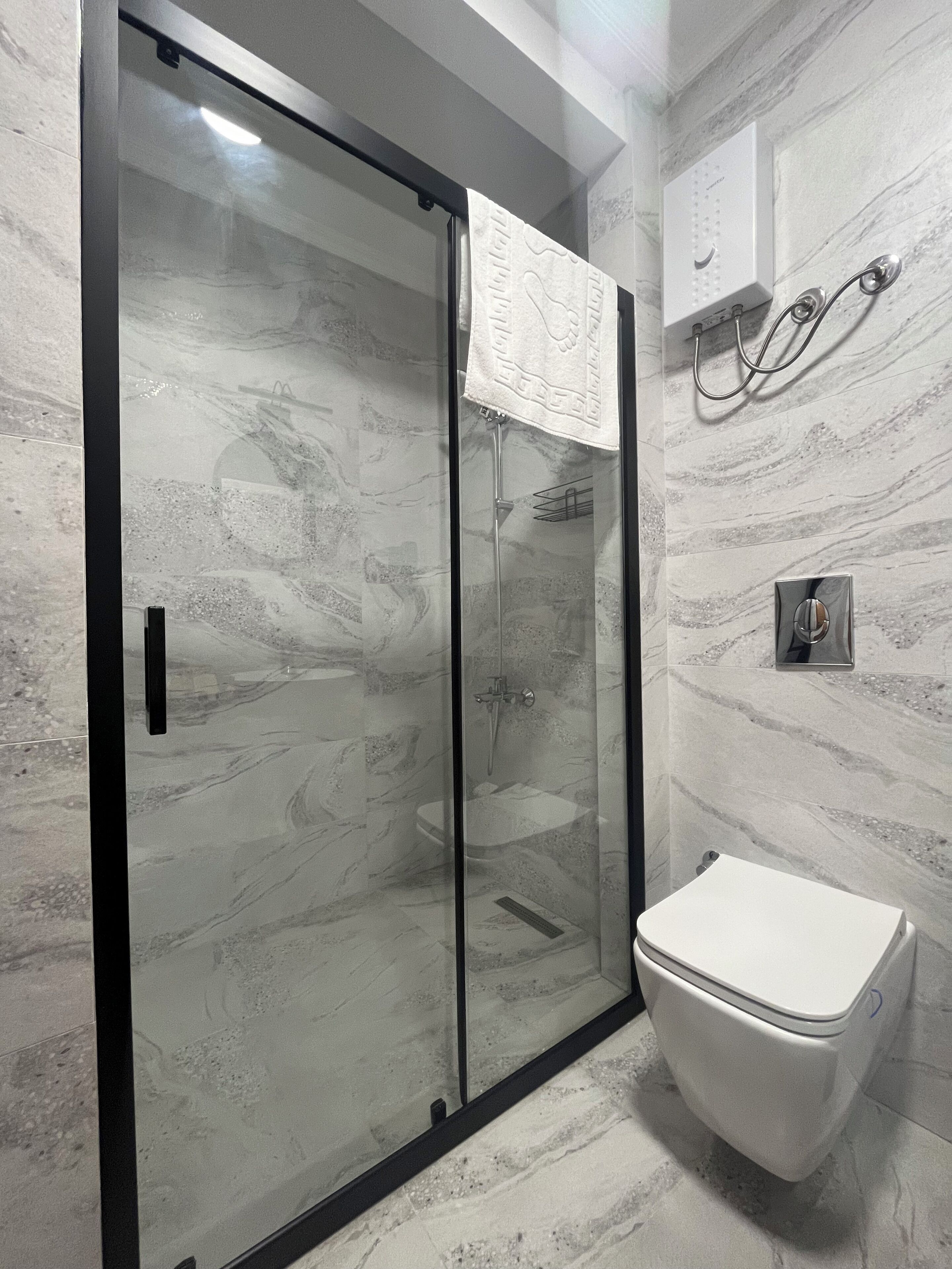 A bathroom with a glass-enclosed shower, a white toilet, and a marble-patterned wall.