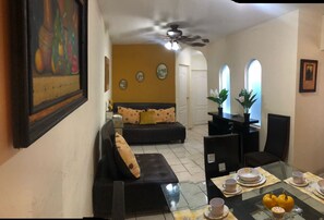 A dining area with a glass table set for four, surrounded by chairs. There is a sofa with polka dot cushions in the background. - Jhon House for 6 people (Tepic)