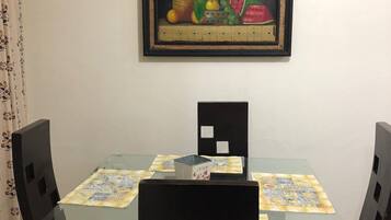 A dining area with a glass table, black chairs, and a framed painting above.
