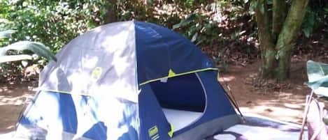 A blue tent set up on a ground tarp in a forested area.