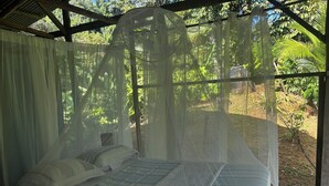 A bed with a canopy in a room with a view of greenery. -  Rio Agujitas Ecolodge Farmand Tour (Drake Bay)